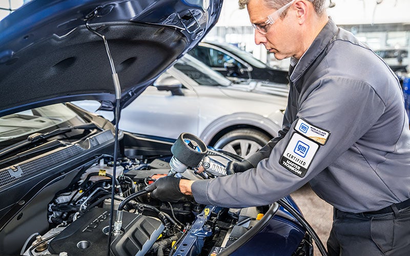 Chevrolet Certified Service technician checking under the hood of a blue SUV