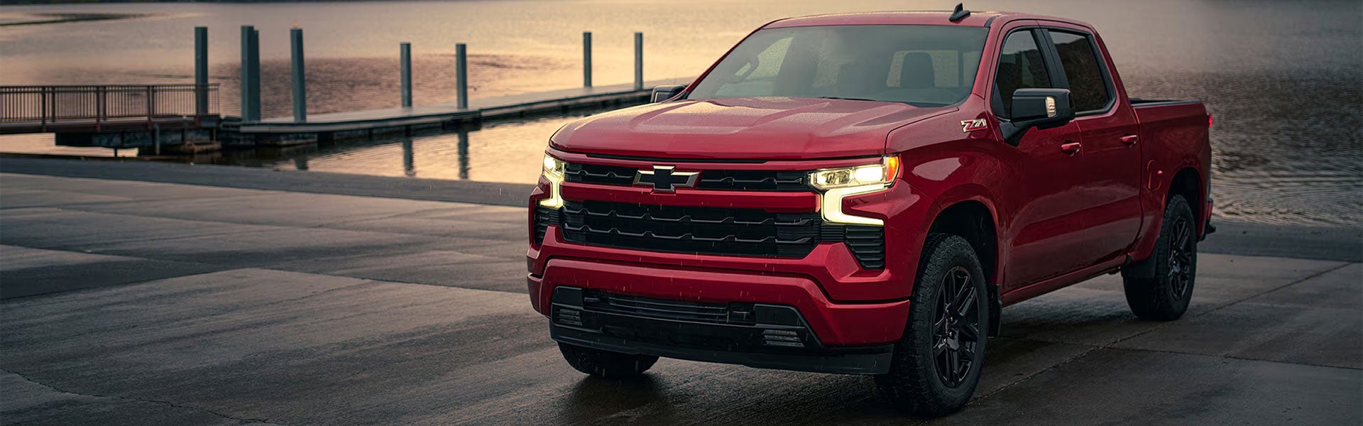 Red Chevrolet Silverado crew cab pickup parked by the water at dusk